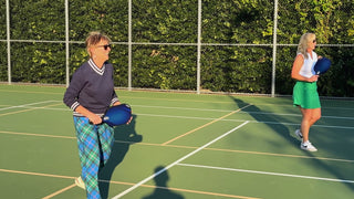 Two people playing pickleball on an outdoor court with a green background.