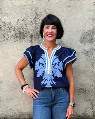 Woman wearing a navy blue top with white floral patterns against a textured wall.