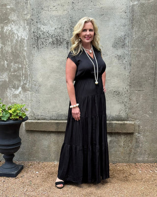 Woman in a black dress standing against a textured wall.