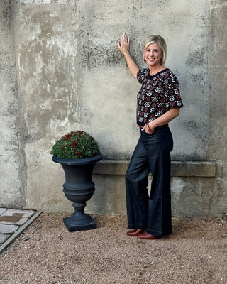 Woman standing next to a stone wall with a decorative urn and plant