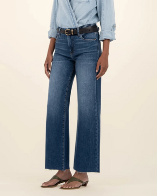 Person wearing a light blue denim shirt and dark blue jeans on a beige background