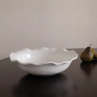 White ceramic bowl with scalloped edge on a dark surface with a pear in the background.