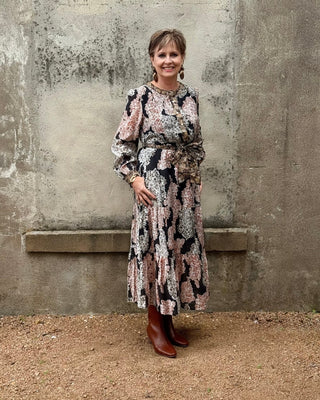 Woman in a patterned dress standing against a textured wall.