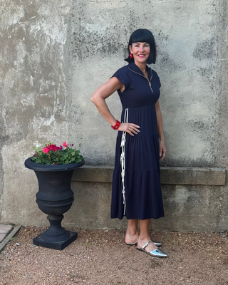 Woman in a navy dress standing next to a stone wall with a flower pot.