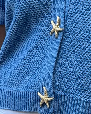 Woman wearing a blue cardigan with starfish buttons against a textured wall.