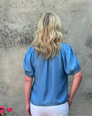 Person wearing a blue blouse standing against a textured wall.