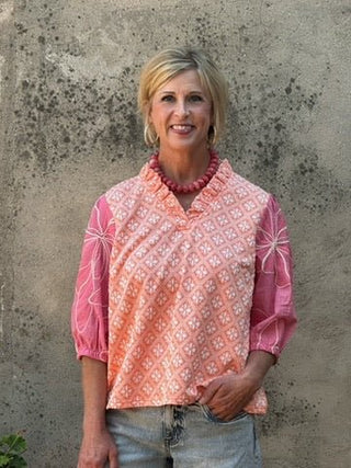 woman standing in ront of a concrete wall wearing jeans and a pink and orange top