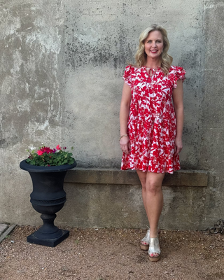 Woman in a red floral dress standing next to a stone wall and flower pot.