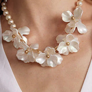 Necklace with white floral pendants and pearl-like beads on a person wearing a white top.