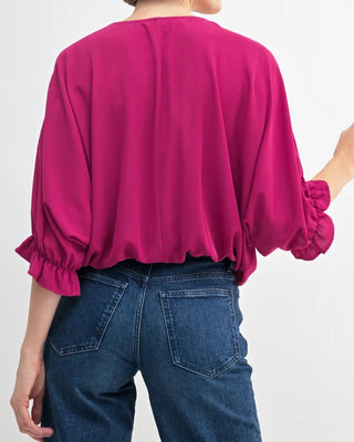 Person wearing a bright pink blouse with balloon sleeves and blue jeans on a white background