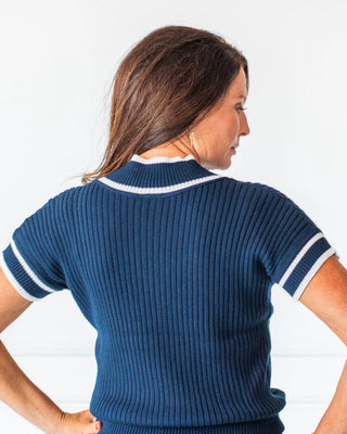 Woman wearing a blue ribbed sweater with white trim against a white background