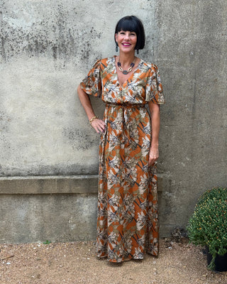 Person wearing a patterned dress standing on a concrete surface with a garden background