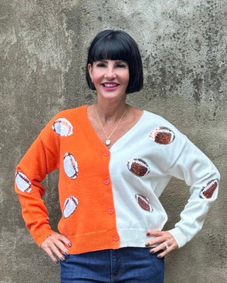 Woman wearing a colorful cardigan with football patterns against a textured wall.
