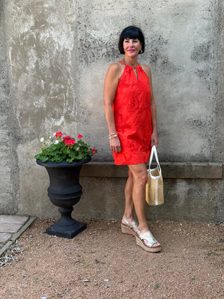 Woman in a red dress standing next to a stone wall with a planter of flowers.
