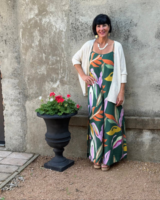 Woman in a colorful dress standing next to a stone wall with a planter of flowers.