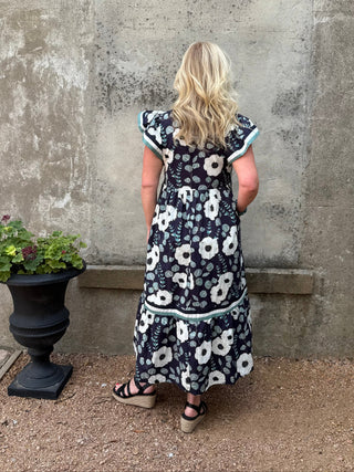 Woman wearing a floral dress standing against a textured wall.
