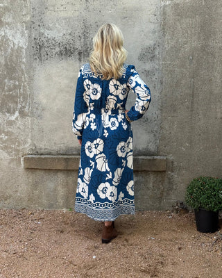 Person wearing a blue floral dress standing on a concrete surface with a textured ground.