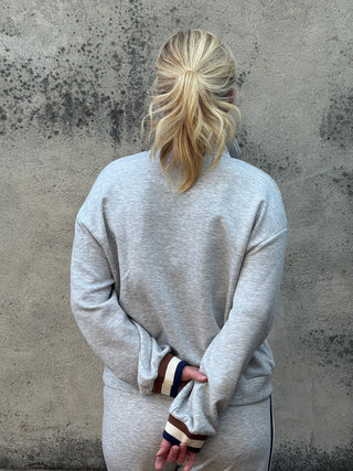 Person wearing a gray sweatshirt with striped sleeves on a concrete floor