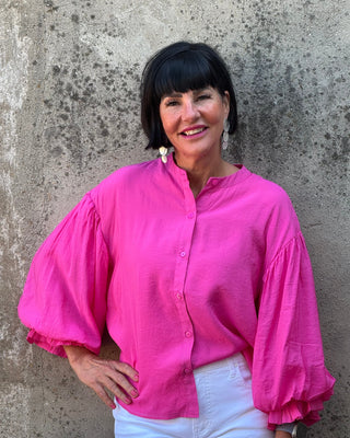 Woman wearing a bright pink blouse with puffed sleeves against a textured wall.