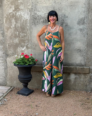 Woman in a colorful dress standing next to a potted plant on a concrete surface.