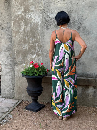 Person holding a colorful floral-patterned bag on a concrete floor with a plant in the background