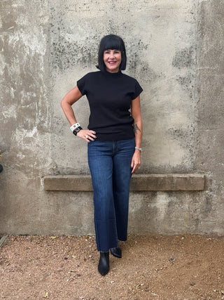 woman against a wall in a short sleeve black sweater and jeans