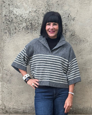 woman against a wall in a  3/4 sleeve greysweater and jeans