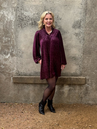 woman in plum dress against a conrete wall