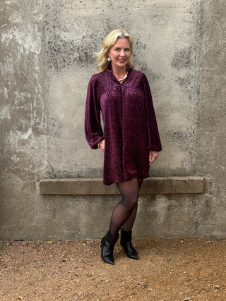 woman in plum dress against a conrete wall