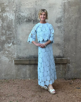 Woman wearing a light blue floral dress standing against a textured wall.
