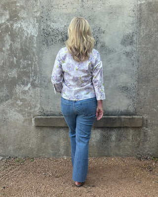 Person wearing a floral shirt and blue jeans standing against a textured wall.