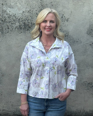 Woman wearing a lavender floral  print blouse by Jodifl and jeans against a textured wall.