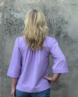 Person wearing a purple shirt and blue jeans against a textured gray wall