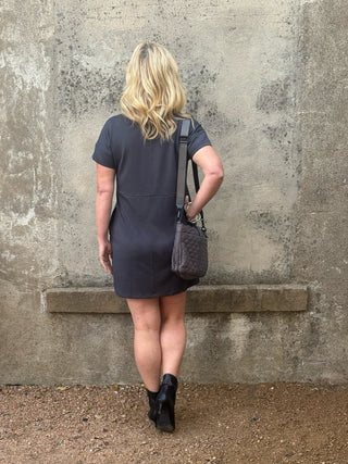 back view of blonde woman in a sporty gry dress, black ankle boots and a scarf up against a concrete wall