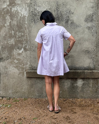 Person wearing a light purple dress standing against a textured wall.