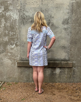 Woman wearing a patterned dress standing against a textured wall.