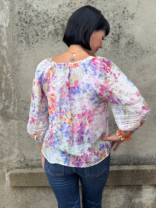 Person wearing a colorful floral blouse against a concrete wall.