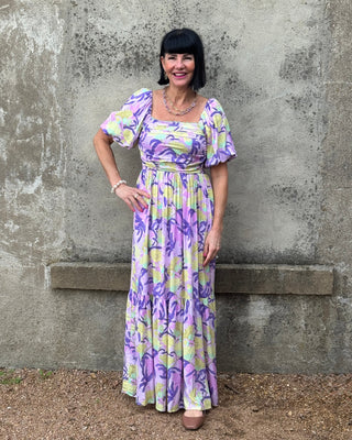 Woman wearing a Lavender floral dress standing against a textured wall.