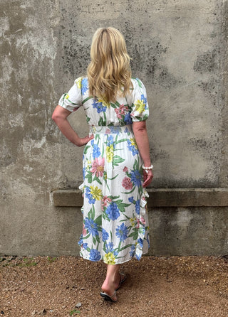 Woman wearing a floral dress standing against a textured wall.