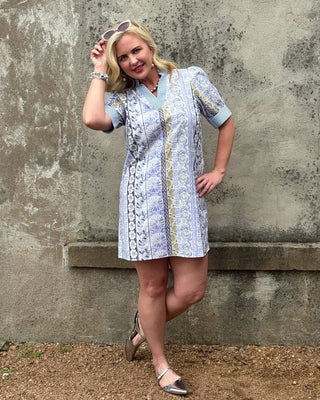 Woman in a patterned dress standing against a textured wall.