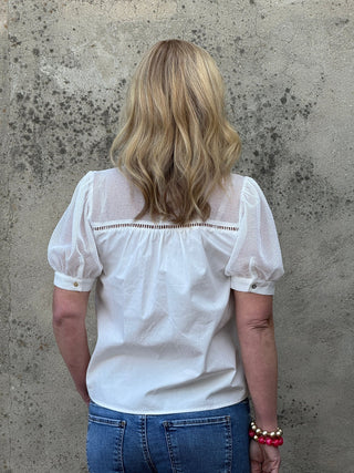 Person wearing a white blouse with lace details on a concrete floor