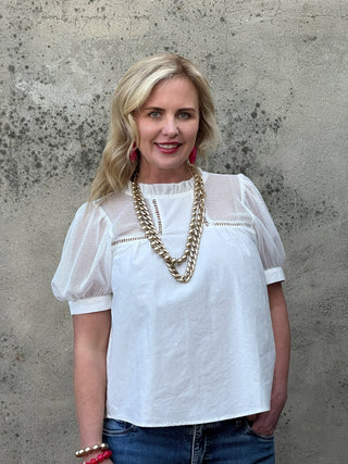 Woman wearing a white blouse with sheer sleeves against a textured wall.