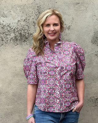 Woman wearing a pink patterned blouse against a textured wall.