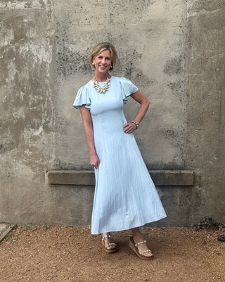 Woman in a light blue dress standing against a textured wall.