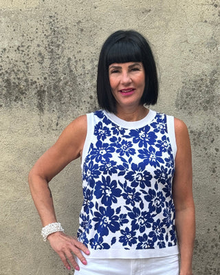 Person wearing a blue floral top and white pants standing on a concrete surface.