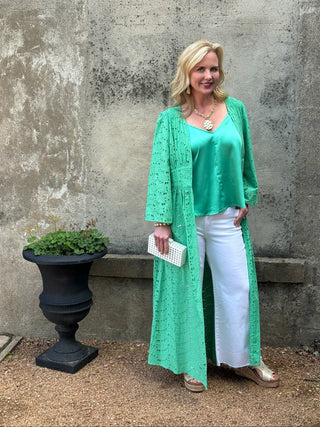 Woman in a green dress standing against a textured wall with a pot of plants.