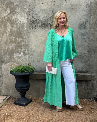 Woman in a green dress standing against a textured wall with a plant.
