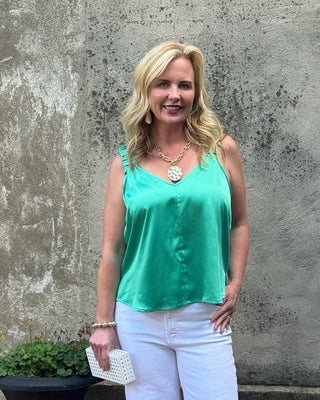 Woman in a green top and white pants standing against a textured wall.