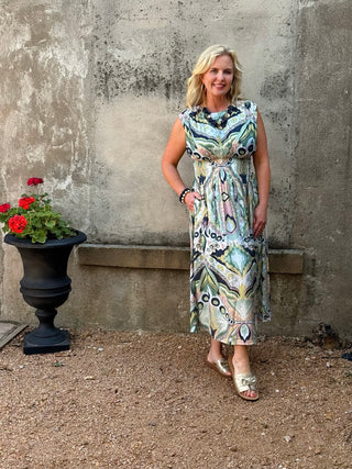 Woman in a patterned dress standing next to a stone wall with a potted plant.