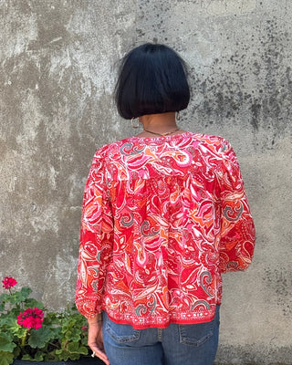 Person wearing a red patterned jacket standing on a concrete surface with a flower pot nearby.